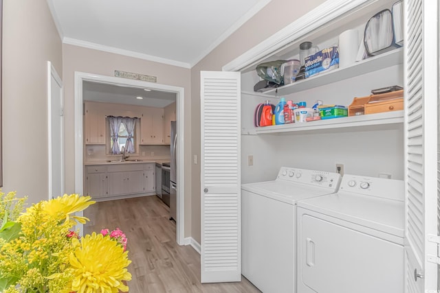 clothes washing area featuring crown molding, sink, washing machine and clothes dryer, and light wood-type flooring