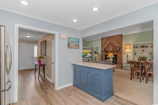 kitchen featuring blue cabinets, stainless steel refrigerator, ornamental molding, kitchen peninsula, and a fireplace