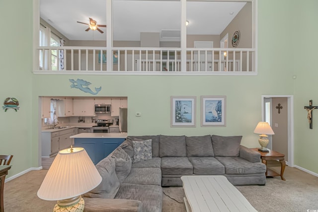 living room with sink, a towering ceiling, light colored carpet, and ceiling fan