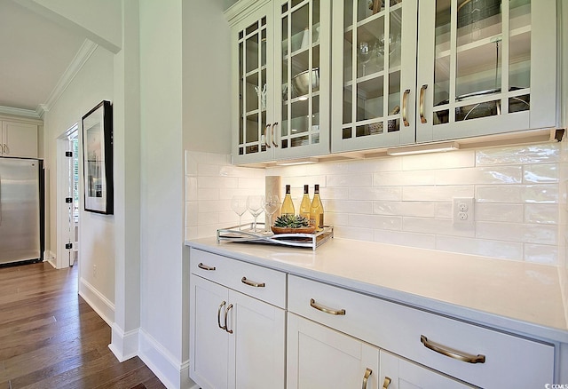 bar with stainless steel refrigerator, ornamental molding, backsplash, white cabinets, and dark wood-type flooring