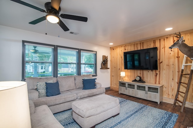 living room with ceiling fan, dark wood-type flooring, and wood walls