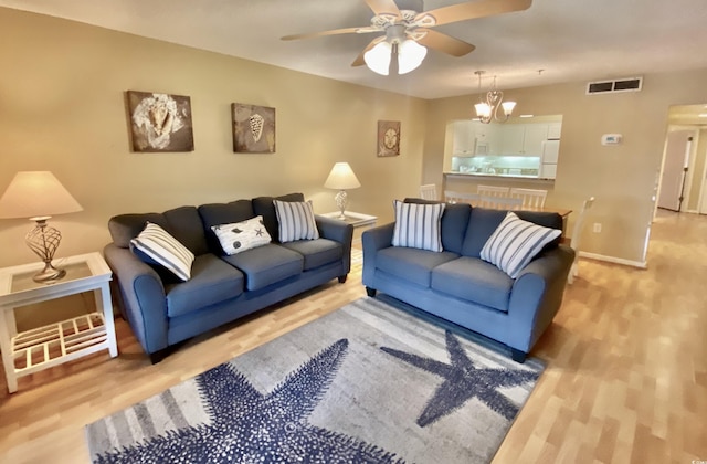 living room featuring ceiling fan with notable chandelier and light hardwood / wood-style flooring