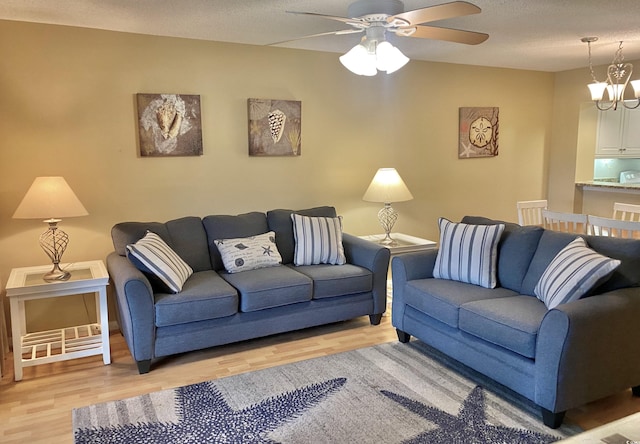 living room featuring ceiling fan with notable chandelier, light hardwood / wood-style floors, and a textured ceiling