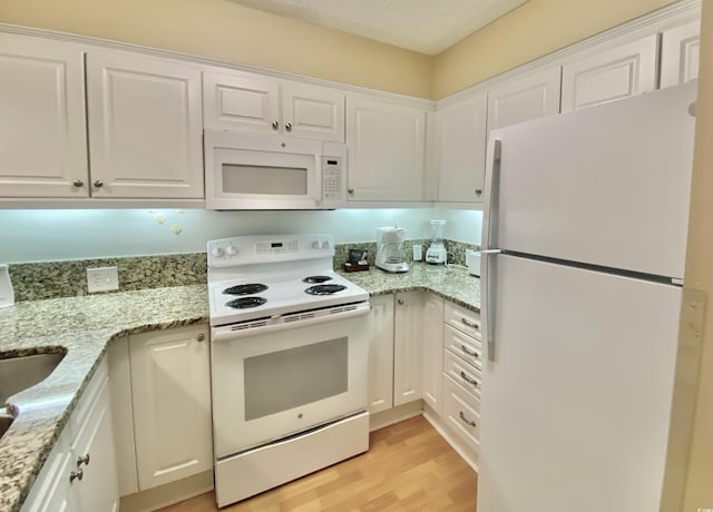 kitchen with white cabinetry, white appliances, light stone countertops, and light hardwood / wood-style floors