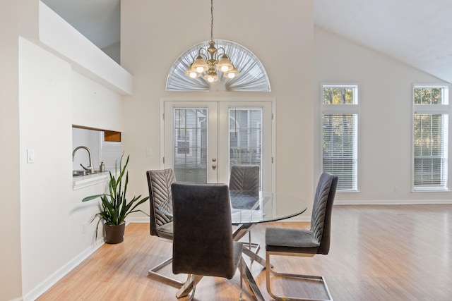 dining area with french doors, high vaulted ceiling, sink, an inviting chandelier, and light hardwood / wood-style flooring