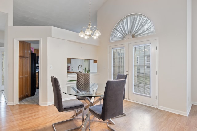 dining space with french doors, light wood-type flooring, vaulted ceiling, and an inviting chandelier