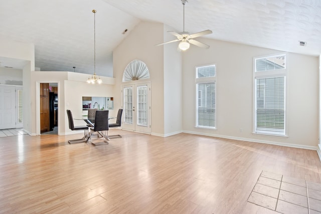 unfurnished living room featuring light hardwood / wood-style floors, ceiling fan with notable chandelier, a textured ceiling, and high vaulted ceiling