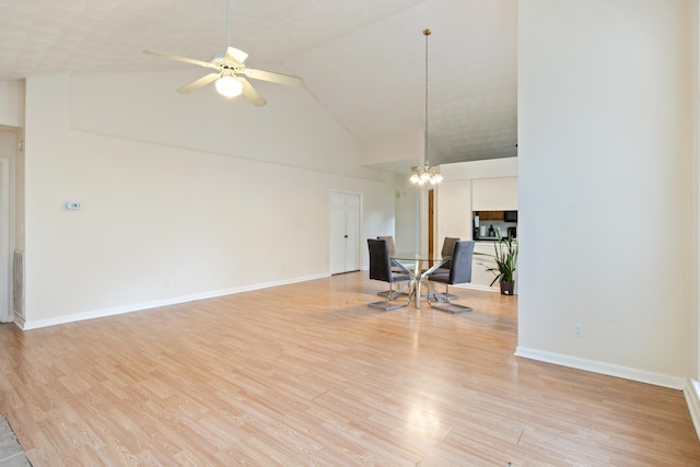 unfurnished living room with high vaulted ceiling, light wood-type flooring, and ceiling fan with notable chandelier