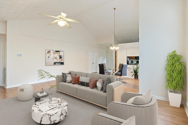 living room with high vaulted ceiling, light hardwood / wood-style floors, and ceiling fan with notable chandelier