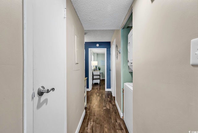 corridor with dark wood-type flooring, stacked washer and clothes dryer, and a textured ceiling