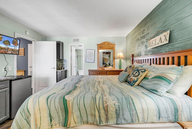 bedroom featuring a textured ceiling, ensuite bath, and stainless steel refrigerator