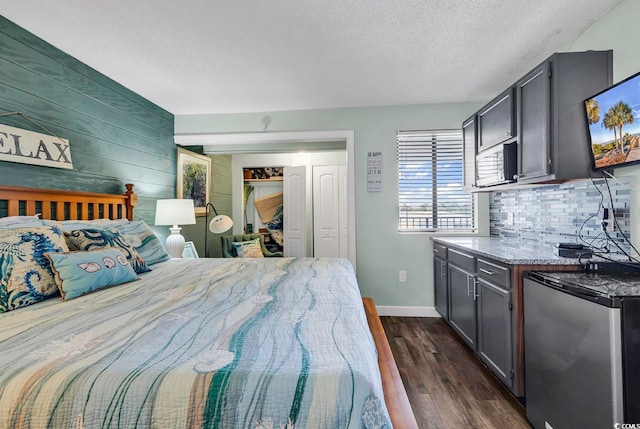 bedroom featuring dark hardwood / wood-style flooring, wooden walls, a textured ceiling, and stainless steel refrigerator