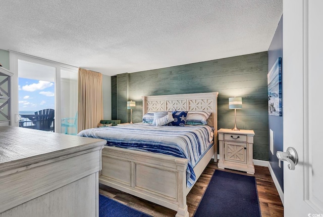 bedroom with a textured ceiling, access to exterior, dark hardwood / wood-style floors, and wooden walls