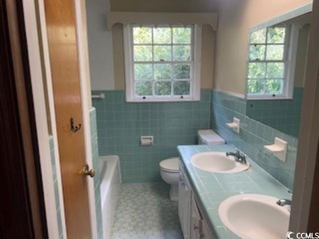 bathroom with tile patterned floors, vanity, toilet, tile walls, and a bath