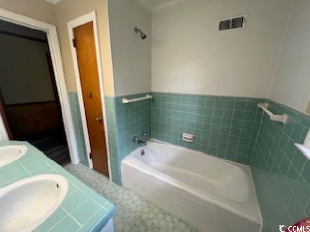 bathroom featuring vanity, a bath, and tile walls