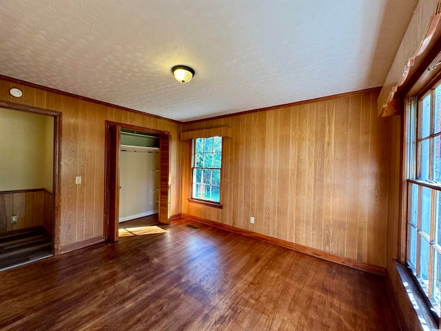 unfurnished bedroom featuring wooden walls, ornamental molding, a closet, a textured ceiling, and dark hardwood / wood-style floors