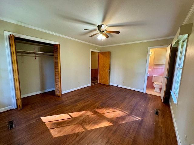 unfurnished bedroom with ceiling fan, dark wood-type flooring, crown molding, ensuite bathroom, and a closet