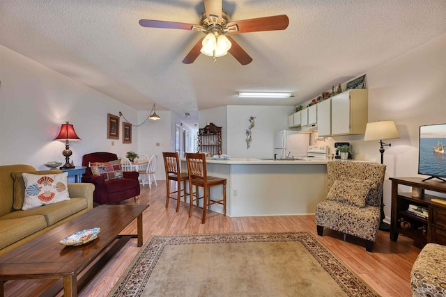 living room featuring ceiling fan, light hardwood / wood-style floors, and a textured ceiling