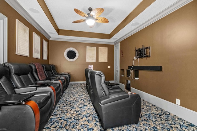 cinema room with a tray ceiling, ceiling fan, carpet flooring, and ornamental molding