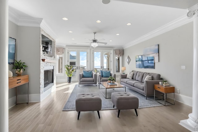 living room with french doors, a stone fireplace, crown molding, ceiling fan, and light hardwood / wood-style floors