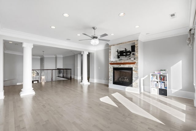 unfurnished living room with ceiling fan, a stone fireplace, ornamental molding, decorative columns, and light wood-type flooring