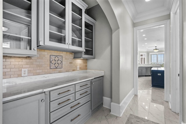 bar with gray cabinetry, decorative backsplash, light stone countertops, and ornamental molding