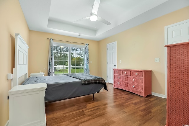 bedroom featuring ceiling fan, dark hardwood / wood-style floors, and a tray ceiling