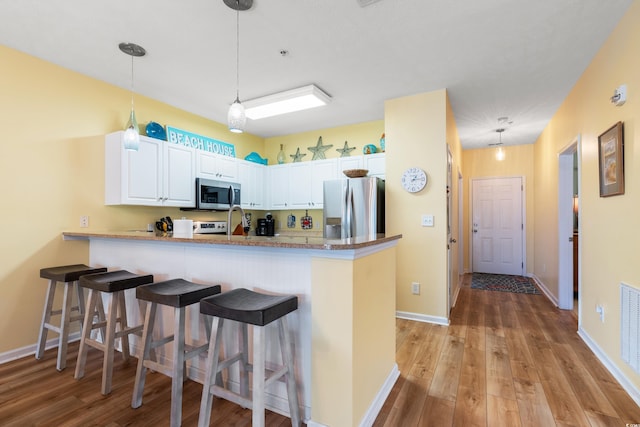 kitchen with white cabinetry, kitchen peninsula, appliances with stainless steel finishes, and hanging light fixtures