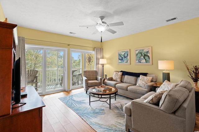 living room with light hardwood / wood-style floors, ceiling fan, and a textured ceiling