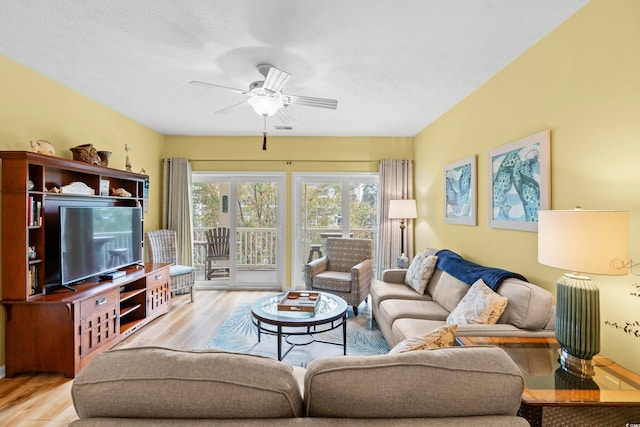 living room featuring a textured ceiling, light wood-type flooring, and ceiling fan