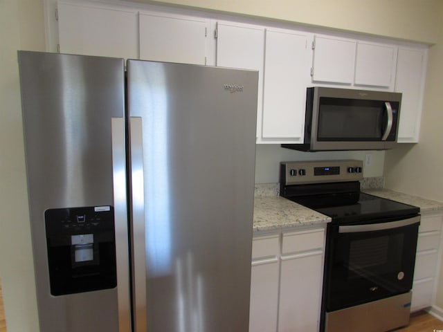 kitchen featuring appliances with stainless steel finishes, white cabinetry, light stone counters, and light wood-type flooring