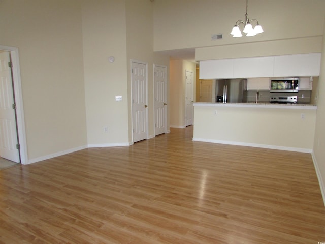 unfurnished living room featuring an inviting chandelier, light hardwood / wood-style flooring, and a high ceiling