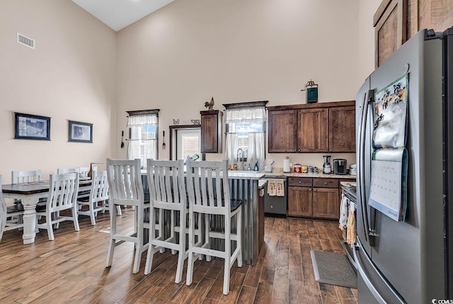 kitchen with appliances with stainless steel finishes, dark hardwood / wood-style flooring, a towering ceiling, a breakfast bar, and a center island