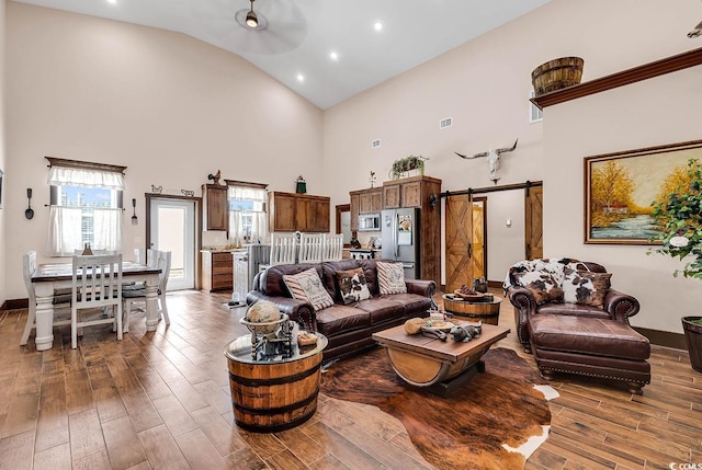 living room with ceiling fan, a high ceiling, and a barn door