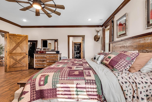 bedroom with ceiling fan, hardwood / wood-style flooring, ornamental molding, a walk in closet, and a closet