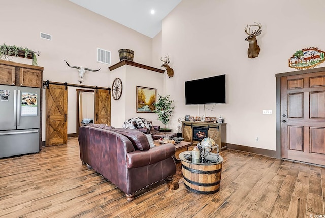 living room featuring high vaulted ceiling, light hardwood / wood-style floors, and a barn door