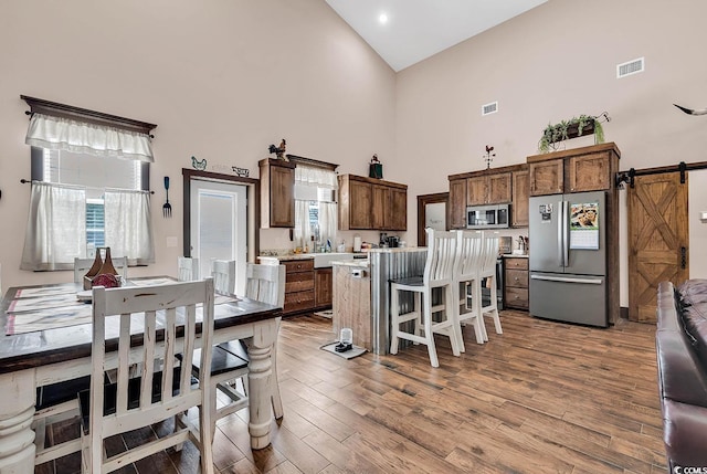 kitchen with a towering ceiling, a kitchen bar, stainless steel appliances, and a barn door