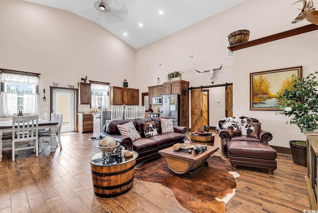 living room with ceiling fan, a barn door, and a high ceiling