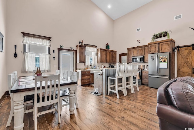 dining room with a towering ceiling, light hardwood / wood-style floors, and a barn door