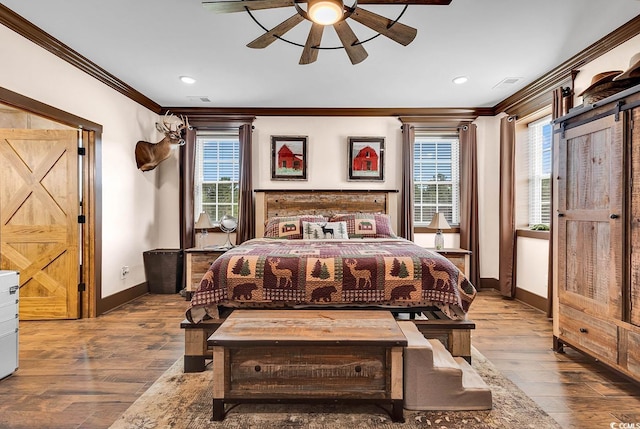 bedroom featuring ceiling fan, a barn door, light wood-type flooring, and crown molding