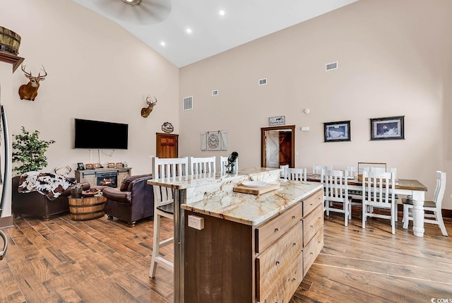 kitchen featuring ceiling fan, a fireplace, a center island, light wood-type flooring, and light brown cabinets