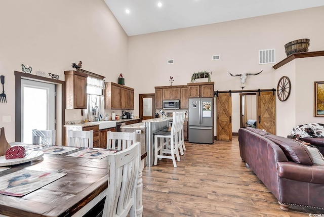 dining room with high vaulted ceiling, light hardwood / wood-style floors, sink, and a barn door