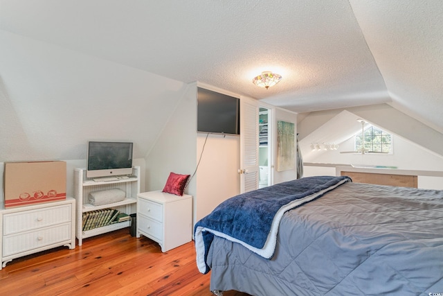 bedroom featuring light hardwood / wood-style floors, a textured ceiling, and lofted ceiling