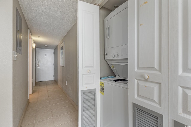 washroom with stacked washing maching and dryer, a textured ceiling, and light tile patterned floors