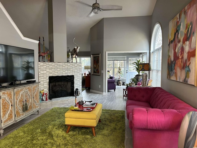 living area featuring a fireplace, a towering ceiling, ceiling fan, wood finished floors, and baseboards