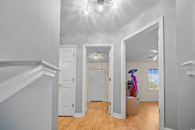 hall featuring a textured ceiling, baseboards, and wood finished floors