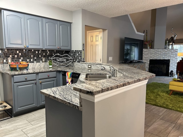 kitchen featuring dishwasher, a tiled fireplace, a peninsula, stone counters, and a sink