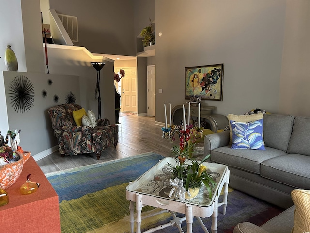 living room featuring a high ceiling, wood finished floors, visible vents, and baseboards