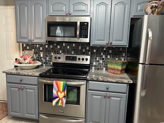 kitchen with appliances with stainless steel finishes, dark stone countertops, gray cabinetry, and tasteful backsplash