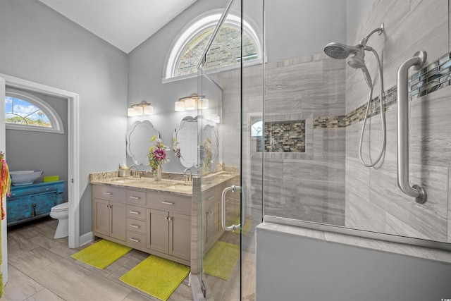 full bath featuring double vanity, a tile shower, a sink, and lofted ceiling